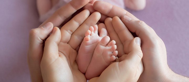 Elternhände halten nackte Babyfüße