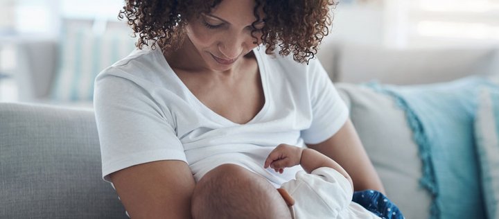 Eine dunkelhäutige Frau hält ihr Baby im Arm und stillt es.