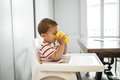 Ein kleiner Junge sitzt im Hochstuhl und trinkt Wasser aus einem gelben Becher.