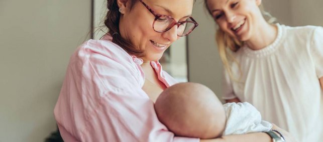 Eine Frau hält ein Baby im Arm, eine andere Frau lächelt dieses an. Eine Frau hält ein Baby im Arm, eine andere Frau lächelt dieses an.