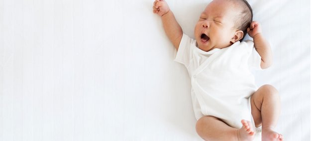 Ein Neugeborenes liegt auf einer weißen Decke und gähnt