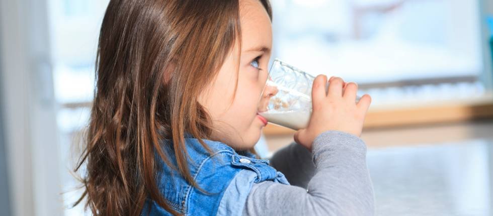 Etwa 3-Jähriges Mädchen trinkt Milch oder Milchalternative aus einem Glas. Sie ist dabei im Profil zu sehen.