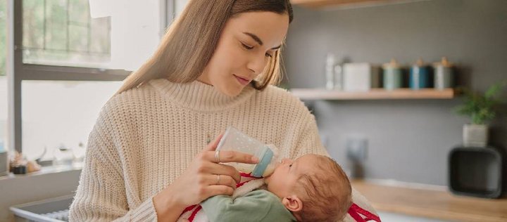 Eine Frau hält ein Baby im Arm und füttert es mit einem Flässchen.