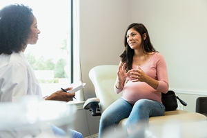 Schwangere spricht lächeln mit Geburtshelferin und bewebt dazu ihre Hände