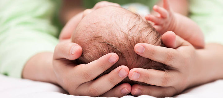 Haende halten Kopf eines Neugeborenen