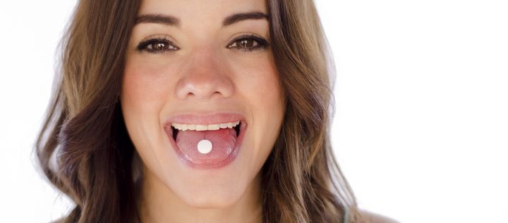 Junge Frau mit Tablette auf der Zunge